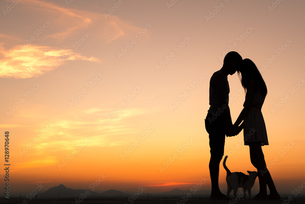 Silhouette of Happy Young Couple playing with cat Outside at Sunset