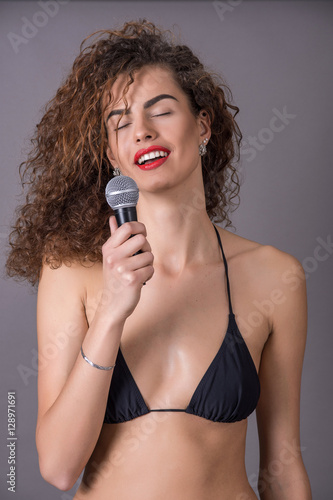 beautiful curly girl in a bikini singing into a microphone