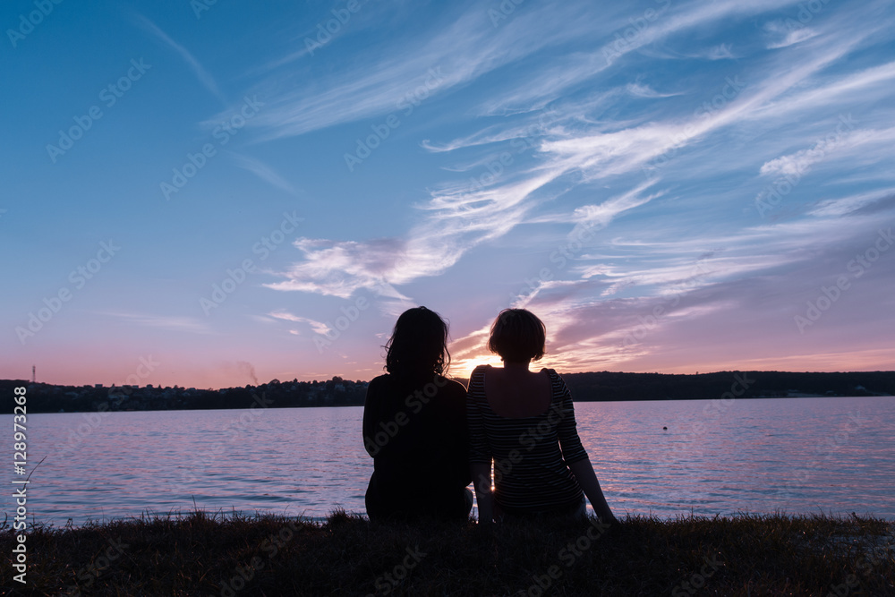 Two women lesbians girlfriend sitting on the shore of the lake a