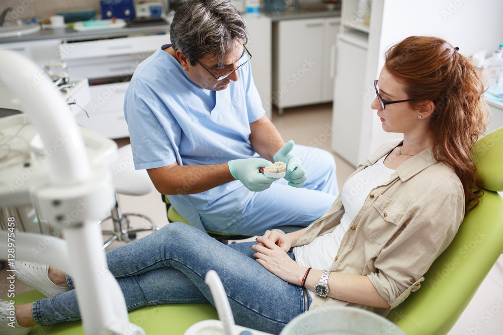 Fototapeta premium Senior male dentist in dental office talking with female patient and preparing for treatment.