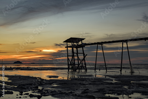 Golden Hour moment,beautiful tropical sunset background, wooden water pump tower on the muddy beach. cloudy and yellow sky.surface level shot.low tide sea view