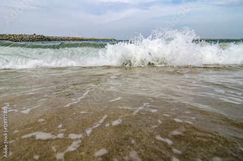 blurred and selective focus image of wave hitting the beach over cloudy and blue sky background