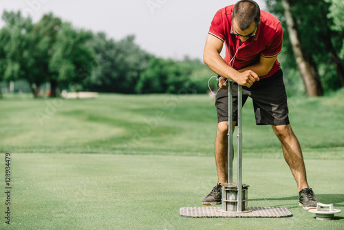 Greenskeeper cutting a golf hole, preparing course photo