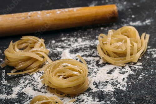 Uncooked rolled traditional italian pasta on wooden background, isolated. Portion of raw fettuccine or tagliatelle or pappardelle. Dry pasta from whole wheat flour. Ingredients for tasty dish