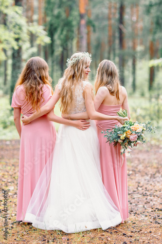 Bride with bridesmaids in the forest. Bride hugging bridesmaids. Bride looking at the camera.