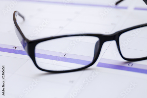 Black male business glasses in office on the desk with calendar as concept of organization and planning. Closeup.