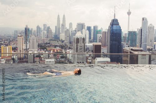 Vacation in Kuala-Lumpur. Young man enjoy swimming in roof top pool with beautiful city view