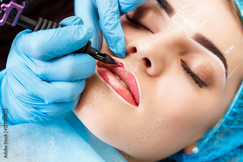 Cosmetologist making permanent makeup on woman's face