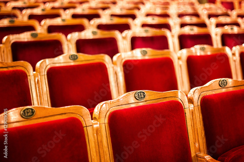 Sets on an empty theatre, taken with selective focus and shallow depth of field. Empty vintage red seats with numbers, teather chair, cinema seats. Movie theater auditorium with lines of red chairs. photo