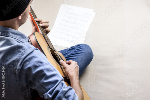 Singer songwriter plays song from sheet music tabs. Male guitar player in jeans  composing a song on acoustic guitar