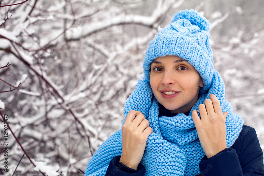 smiling girl in a knitted blue scarf, and cap stands smiling girl in a knitted blue scarf, and cap stands