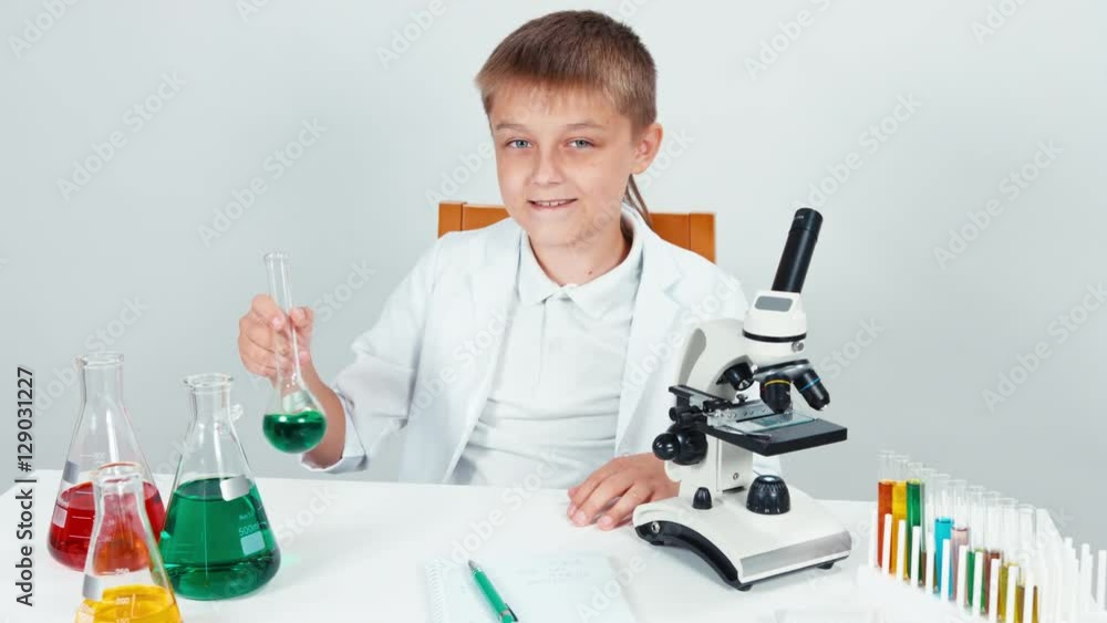 Portrait young chemist mixing chemicals. Schoolboy holding flask. Child sitting at the table isolated on white Portrait young chemist mixing chemicals. Schoolboy holding flask. Child sitting at the table isolated on white