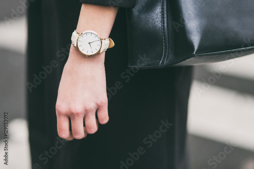 close up fashion details, young business woman holding her black elegant bag. wearing golden and white watch. ideal fall outfit accessories.