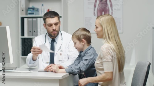 Male Doctor Writes a Prescription to a Young Boy and His Motherand. Gives Prescriptionto Mother with Some Oral Recommendations. Shot on RED Cinema Camera in 4K (UHD). photo