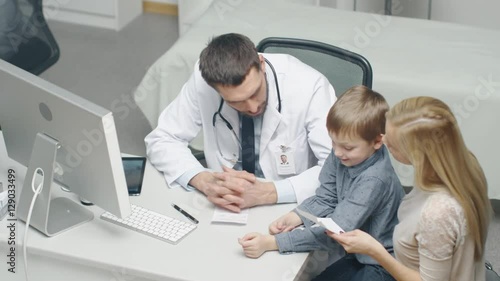 Male Doctor Writes a Prescription to a Young Boy and His Motherand. Gives Prescriptionto Mother with Some Oral Recommendations. Shot on RED Cinema Camera in 4K (UHD). photo