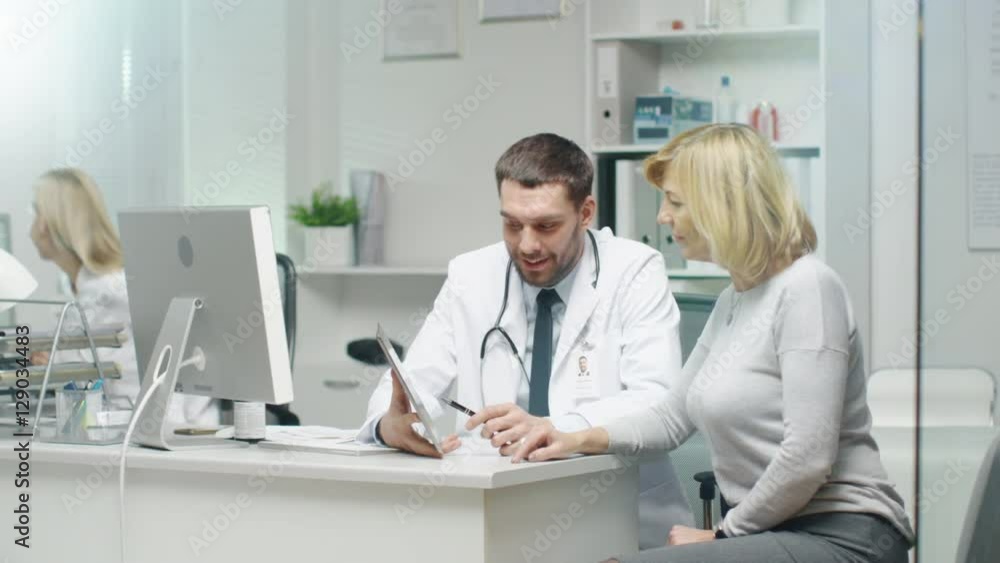 Professional Doctor Consults Mid Adult Woman. He Points out Something on the Screen to Her. Nurse Puts Documents on Doctor's Table. Shot on RED Cinema Camera in 4K (UHD). Professional Doctor Consults Mid Adult Woman. He Points out Something on the Screen to Her. Nurse Puts Documents on Doctor's Table. Shot on RED Cinema Camera in 4K (UHD).