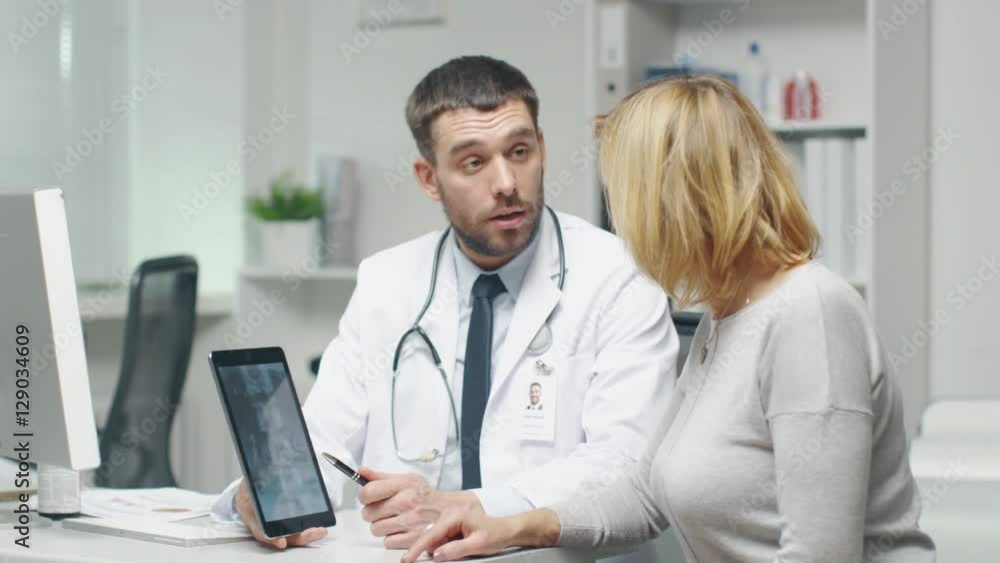 Professional Doctor Consults Mid Adult Woman. He Points out Something on the Screen to Her. They Both Laugh. Shot on RED Cinema Camera in 4K (UHD). Professional Doctor Consults Mid Adult Woman. He Points out Something on the Screen to Her. They Both Laugh. Shot on RED Cinema Camera in 4K (UHD).