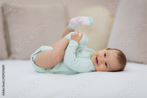Playful baby lying down in bed / Happy baby lying on white sheet and holding her legs