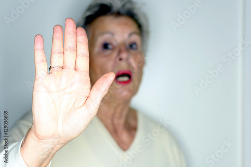 senior woman with her hands signaling to stop over light background 