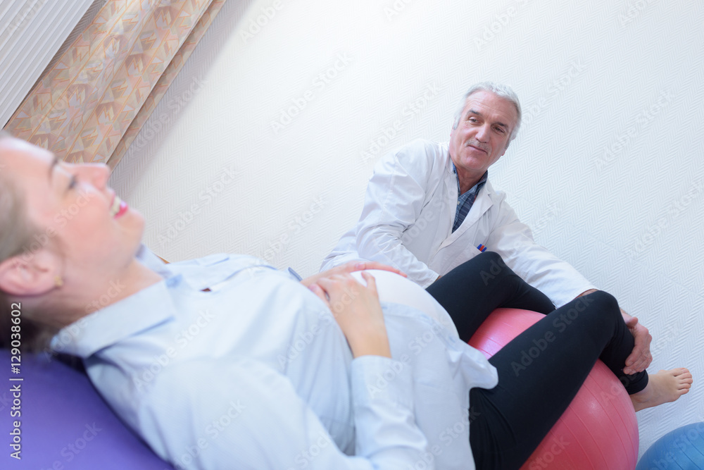 Obraz premium old male doctor with pregnant woman sitting on fitness ball