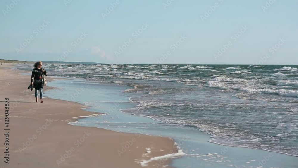 An attractive blond woman in a striped cardigan and jeans is walking on a sandy beach An attractive blond woman in a striped cardigan and jeans is walking on a sandy beach