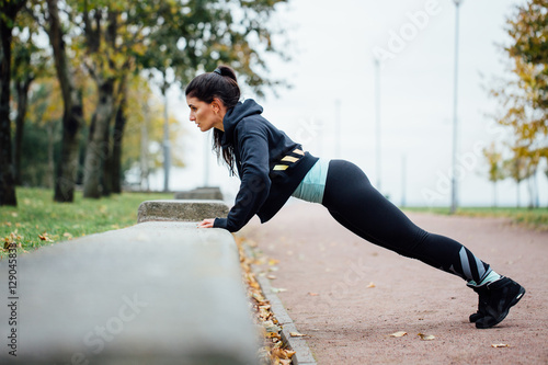 Portrait of woman in sportswear, doing fitness push-ups exercise at fall park, outdoor.