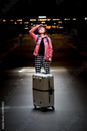 Mature Asian woman with suitcase looking upward to source of con