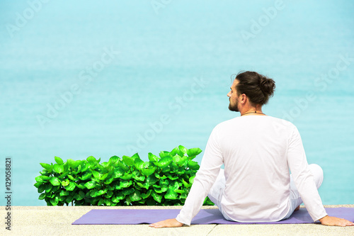 Man in white clothes meditating yoga on the sea shore
