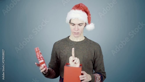 Young man in Santa hat opening a gift box with a surprise inside seeing Fuck You sign photo