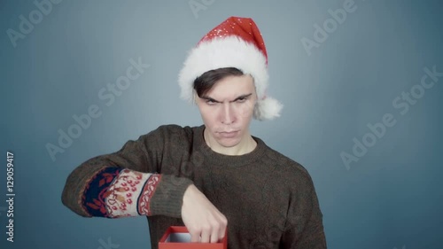 Young man in Santa hat opening a gift box with a surprise inside seeing little red package photo