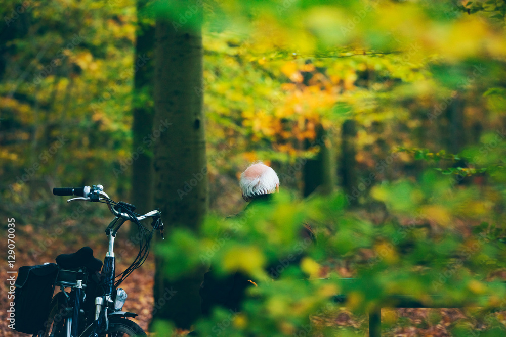 Naklejka premium Senior man with bicycle resting on bench in autumn forest.