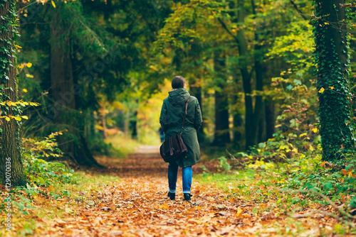 Woman with shoulder bag walking on path in autumn forest. © ysbrandcosijn