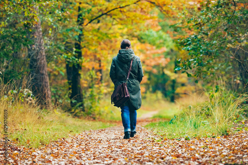 Woman with shoulder bag walking on path in autumn forest.
