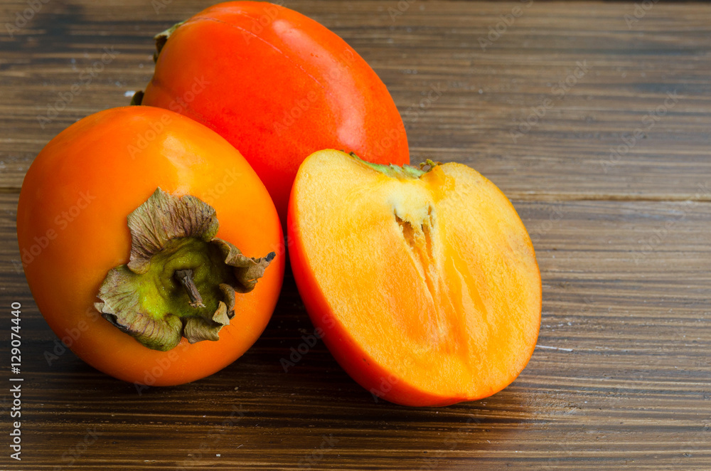Close up of fresh organic persimmon fruit cut in half on rustic wood background. Concept for healthy food, vegan or raw diet.Copy space. Close up of fresh organic persimmon fruit cut in half on rustic wood background. Concept for healthy food, vegan or raw diet.Copy space.