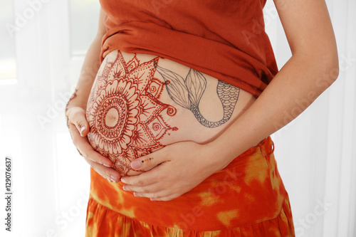 Young pregnant woman with henna tattoo on belly on light background