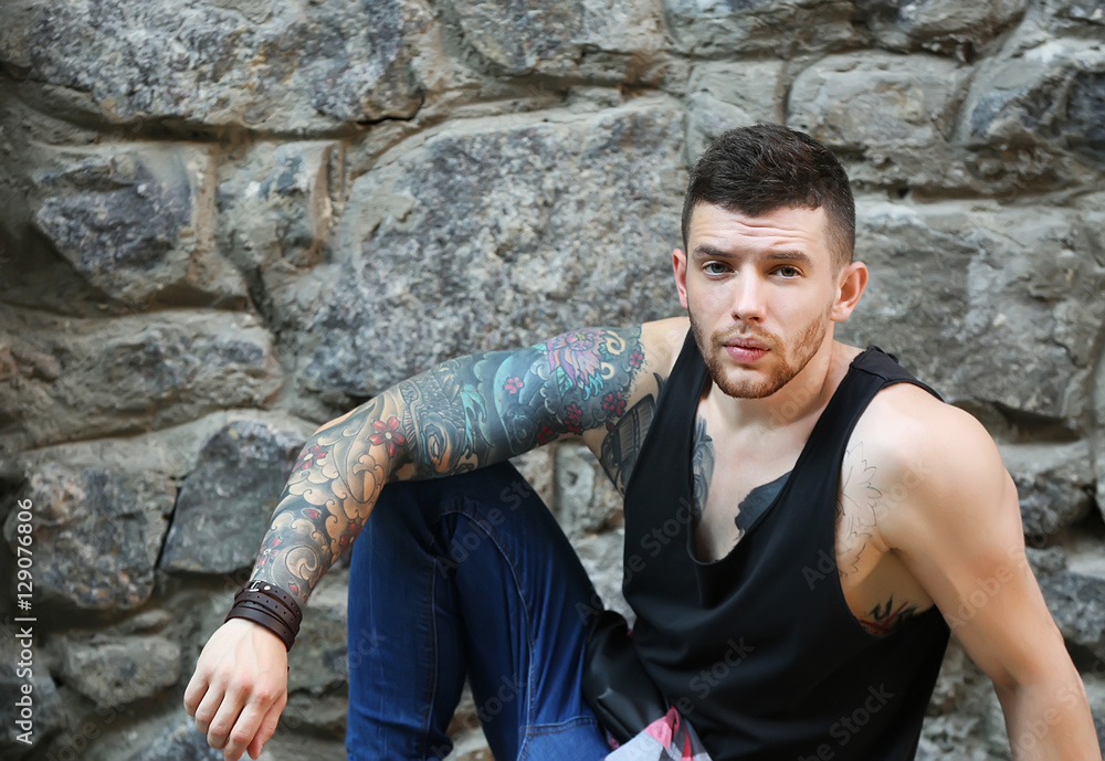 Young tattooed man posing on stone wall background Young tattooed man posing on stone wall background