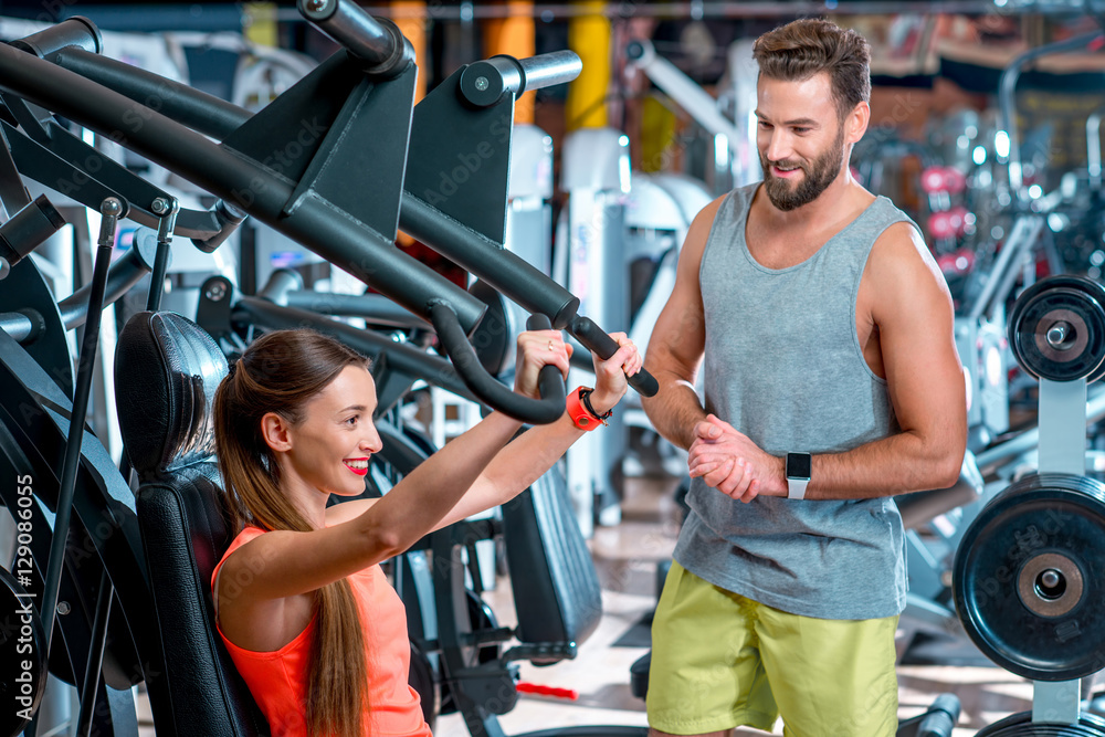 Young woman with personal trainer exercising on the simulator in the gym. Sport couple training together Young woman with personal trainer exercising on the simulator in the gym. Sport couple training together