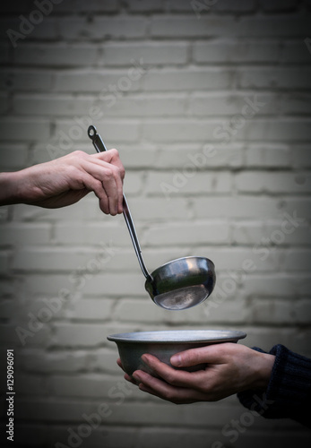 Homeless. In the hands of one man metal plate. In the hand of another person ladle.
