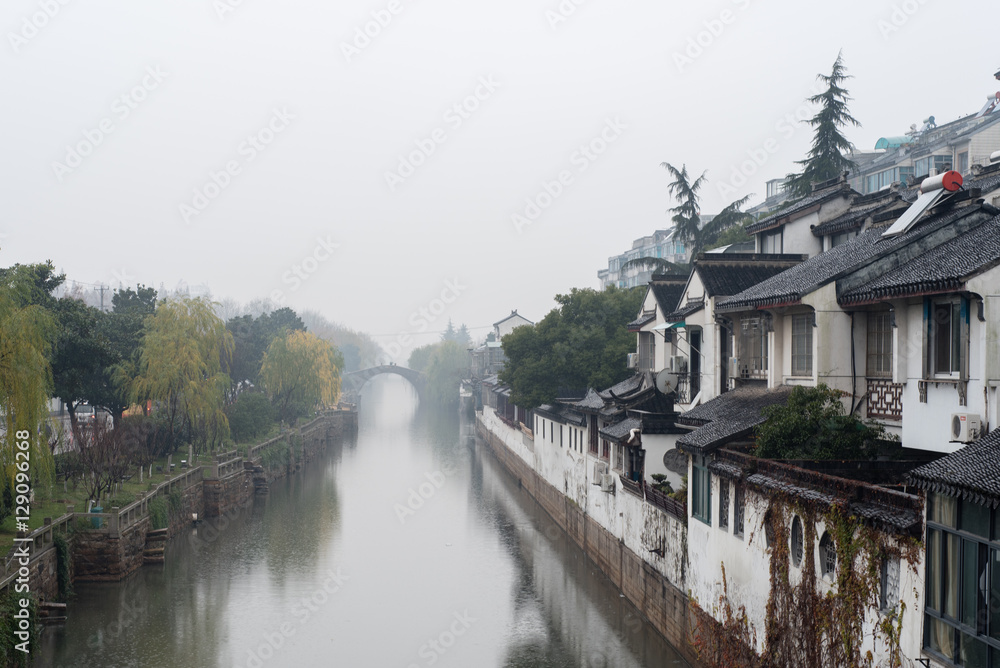 Canal in Suzhou lined by trees and traditional buildings Canal in Suzhou lined by trees and traditional buildings