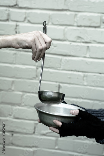 Homeless. In the hands of one man metal plate. In the hand of another person ladle. 