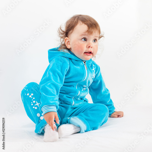 Charming baby in blue sits on floor looking away