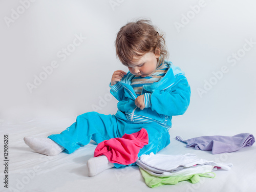 Charming baby in blue playing with baby clothes
