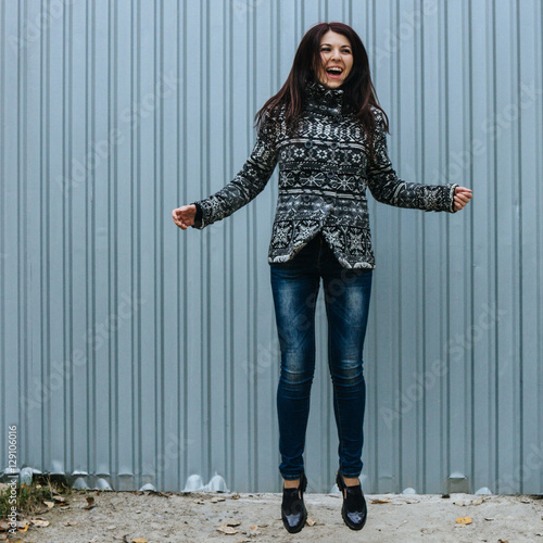Beautiful young woman in casual clothes jumping against the fence