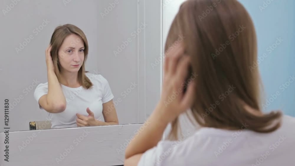 Young pretty woman fixing her hair in front of the mirror. White interior, makeup room Young pretty woman fixing her hair in front of the mirror. White interior, makeup room