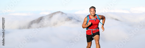 Trail runner man athlete running in mountains outdoor nature with mountain peak in clouds in background. Panorama horizontal banner landscape crop for copyspace.