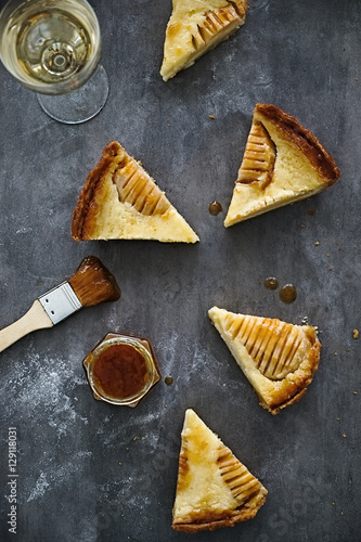 Pieces of pear almond cream tart with glass of white wine and jam. Flat lay. Dark grey background. Food photography
