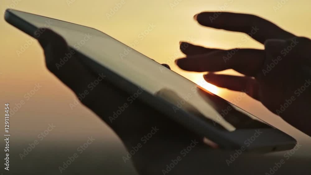 Female silhouette using a digital tablet. Close up shot of woman hands with pad. Sunset light, sun lens flares, golden hour. Relax, nature and technology concept. Close up shot Female silhouette using a digital tablet. Close up shot of woman hands with pad. Sunset light, sun lens flares, golden hour. Relax, nature and technology concept. Close up shot
