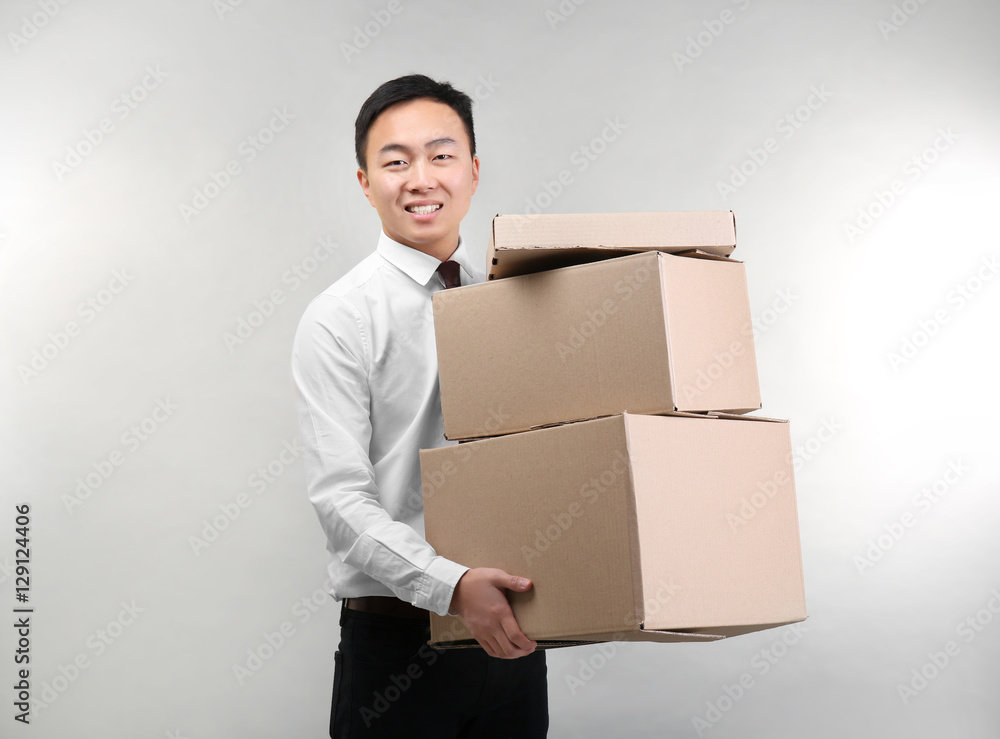 Handsome Asian man with cardboard boxes on light background Handsome Asian man with cardboard boxes on light background