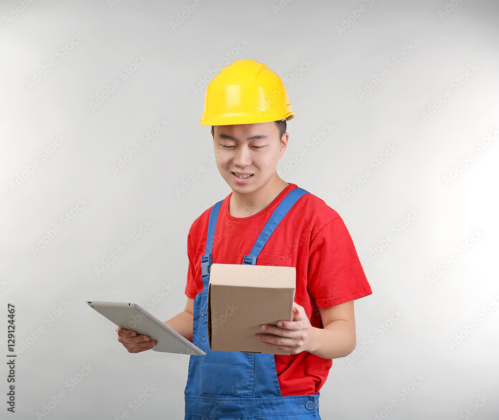 Asian warehouse worker with tablet computer and cardboard box, on light background Asian warehouse worker with tablet computer and cardboard box, on light background