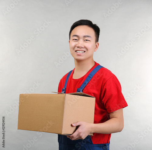 Asian warehouse worker with cardboard box on light background